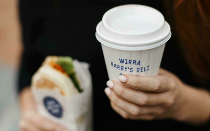 A woman holds a takeaway coffee cup and toasted panini