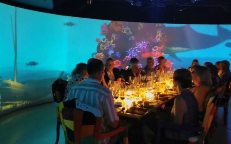 Guests sitting at a dinner table in the 360° audio visual room with underwater scene in background