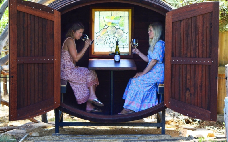Two ladies drinking wine inside a giant wine barrel tasting pod
