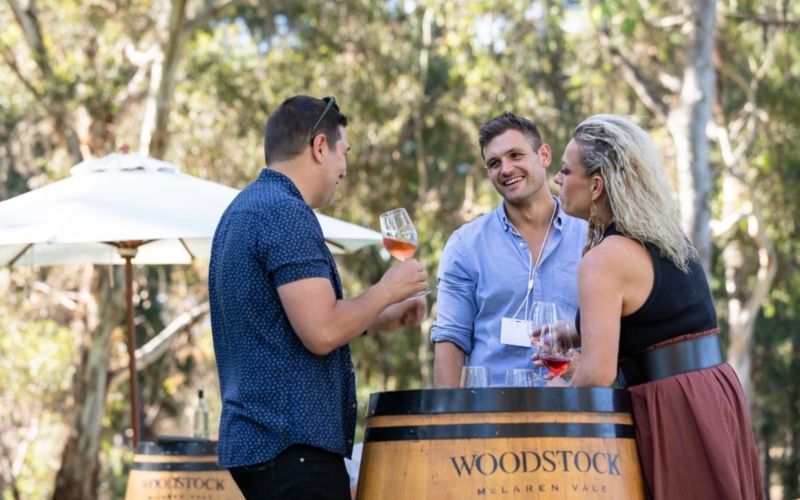 Three people drinking wine around a barrel in the Woodstock gardens