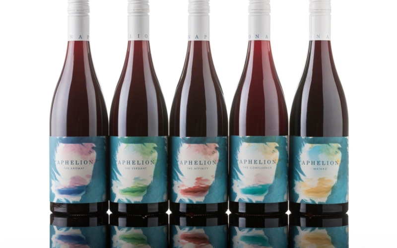 Lineup of five Aphelion wine bottles with distinct blue feather labels and their reflections