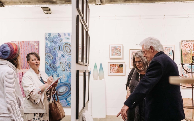 4 people looking at either side of a hanging panel in an exhibition of art woks on a wall